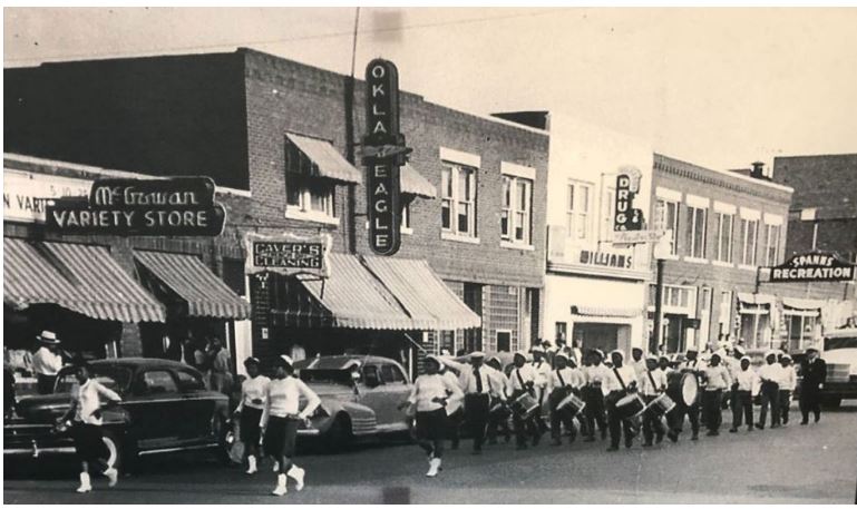Historical photograph of a Black community marching band on an Oklahoma street, with storefronts including the Oklahoma Eagle newspaper visible in the background